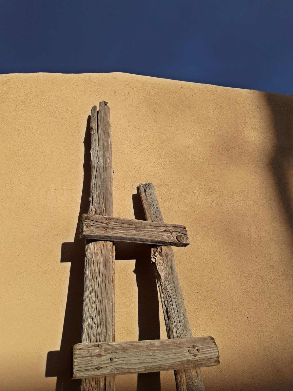 A weathered wooden ladder resting against a sunlit adobe wall